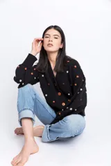 Cárdigan negro de lana con pompones blancos y marrones, escote en V, cierre frontal con botones de madera, mangas largas abullonadas y puños acanalados.