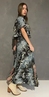 Vestido largo con escote en V tanto en el frente como en la espalda, mangas cortas amplias y corte elastizado debajo del busto. Presenta un estampado de estilo paisley y guardas geométricas en tonos azules, negros y corales.
