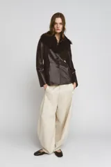 Pantalón de tiro medio color beige claro, de pierna ancha y corte balloon. Presenta pliegues frontales y bolsillos delanteros ocultos en costura.