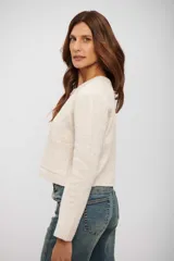 Saco de punto color beige, con cuello redondo, cierre frontal de botones oscuros y dos bolsillos delanteros. De corte recto y manga larga.