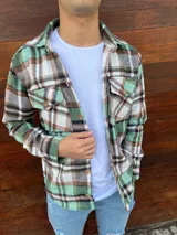 Sobrecamisa de paño con estampado a cuadros en tonos verde, marrón y blanco. Presenta cuello clásico, cierre frontal con botones y dos bolsillos delanteros con solapa y botón.