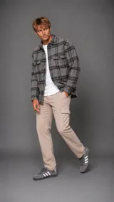 Camisa tipo overshirt de manga larga con diseño a cuadros en tonos gris, verde y naranja. Presenta cuello clásico, cierre frontal con botones y dos bolsillos frontales con solapa en el pecho.