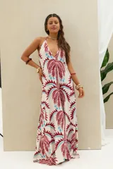 Vestido largo de diseño holgado, con estampado de palmeras en tonos bordó y celeste sobre base cruda. Presenta escote halter profundo y tirantes finos que se atan al cuello.