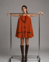 Sacón tejido en lana merino de color naranja, con cuello chal acanalado, bolsillos frontales con detalles en cuero y cierre de botones tipo duffle con presillas de cuero.