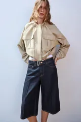 Cazadora color beige con capucha ajustable, manga larga con puño elástico, bolsillos frontales con solapa, bajo ajustable y cierre frontal con cremallera y botones a presión.