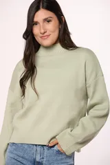 Buzo tejido de punto en color blanco crema, con cuello redondo alto y mangas largas con puños acanalados.