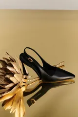 Sandalia pump de cuero color negro, con diseño destalonado, punta fina, taco alto y tira ajustable con hebilla metálica dorada en el lateral.