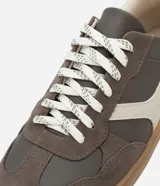 Championes de estilo deportivo tipo chutera, confeccionados en poliuretano con recortes en contraste. Presentan punta redondeada, cordones bicolores y suela plana color caramelo.