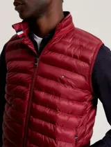 Chaleco acolchado rojo con cierre de cremallera, cuello alto y dos bolsillos laterales con cremallera. Tiene logo de Tommy Hilfiger bordado en el pecho.