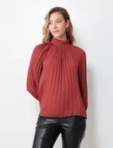 Blusa color ladrillo de gasa plisada con cuello alto, manga larga abullonada con puño y botón de ajuste. Espalda con abertura ojal y doble abotonadura.