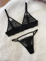 Conjunto de lencería de encaje negro, compuesto por un top tipo bralette con tiras decorativas sobre las copas y una bombacha tipo tanga colaless regulable.