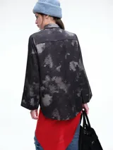 Camisa oversize de lyocell con estampado orgánico efecto lavado. Presenta cuello clásico, cierre frontal con botones, mangas amplias con puños anchos y un diseño de corte relajado con ruedo asimétrico, siendo más largo en la parte posterior.