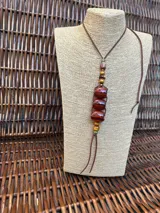 Colgante largo con cordón de cuero marrón y cuentas de piedra en tonos tierra, incluyendo cuentas cilíndricas y esféricas con vetas naturales.