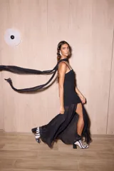 Vestido largo negro confeccionado en crepé y gasa, de corte al cuerpo con escote recto, tiritas finas y falda larga semitransparente con tajo lateral pronunciado. Incluye accesorio tipo corbatín a juego.