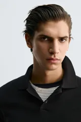 Polo de punto de manga larga con cuello solapa y cierre frontal de botones. Presenta un diseño de corte regular con aberturas laterales en el bajo.