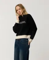 Buzo Rip Curl de punto color negro con diseño de bloques de color, presenta paneles en color crudo en los puños, cuello y el borde inferior. Incluye la inscripción "Rip Curl" bordada en el pecho con tipografía estilo gótico.