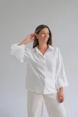 Camisa blanca de corte holgado con cuello clásico, cierre frontal de botones y mangas tres cuartos con sutil detalle bordado en los puños.