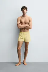 Bañador corto de hombre color amarillo pálido, confeccionado en tejido técnico con acabado aterciopelado. Presenta cintura elástica ajustable con cordón, bolsillos laterales y un bolsillo trasero de plastrón con solapa. Incluye forro interior.