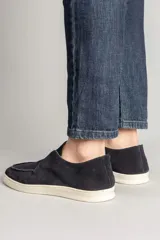 Botineta masculina de gamuza en color azul marino, con diseño slip-on sin cordones y suela de goma blanca. Presenta costuras visibles en la puntera y un estilo urbano minimalista.