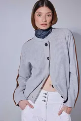 Saco de punto acanalado en color gris claro, con cierre frontal de botones oscuros. Presenta un diseño de bloques de color en las mangas, combinando negro y marrón, y un cuello redondo.