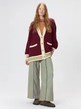 Cardigan de tejido de punto con diseño de ochos, corte oversize y mangas largas con puños acanalados. Presenta un escote en V con solapas en contraste, cierre frontal con botones y dos bolsillos delanteros con bordes en contraste. El diseño incluye detalles de rayas en los puños y en el ruedo.