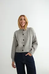 Cardigan de punto gris con cuello redondo, cierre frontal de botones y diseño de costuras visibles en el frente. Posee puños y ruedo acanalados.