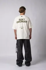 Remera de corte oversize color negro, confeccionada en algodón premium. Presenta un diseño gráfico minimalista estampado en el frente con tipografía y logotipos en color crema.