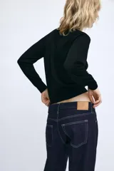 Jeans de tiro medio confeccionados en denim azul oscuro, con diseño de cinco bolsillos, trabillas para cinturón y bajo deshilachado. Cierre frontal con cremallera y botón metálico.