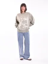 Buzo de cuello redondo y manga larga, color marrón, con estampado gráfico frontal en color lila que incluye texto y personajes animados.