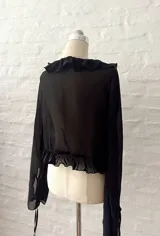 Blusa corta negra de mangas largas acampanadas, con volados en el escote y lazo ajustable en el frente.