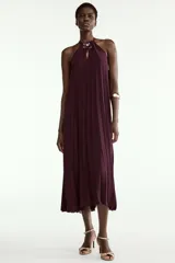 Vestido midi plisado color bordó, con cuello halter, broche de flor en el delantero y anudado en la espalda. Cuenta con forro interior.