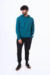 Buzo tipo canguro con capucha y cordones ajustables, confeccionado en felpa color beige. Presenta un pequeño logo bordado en el pecho y una etiqueta decorativa en el puño de la manga.