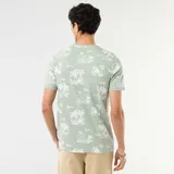 Camiseta verde claro con cuello redondo, manga corta y estampado all-over de estilo tropical con palmeras y paisajes costeros.