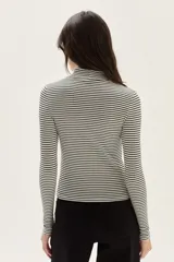 Polera de manga larga con cuello alto, confeccionada en tejido de punto acanalado con diseño de rayas horizontales en color marrón y turquesa. Presenta un bordado pequeño en el pecho y un calce ajustado al cuerpo.