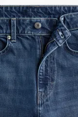 Pantalón jean de denim azul, tiro alto, con diseño wide leg de cinco bolsillos y cierre frontal con botón y cremallera.