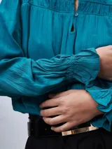 Blusa turquesa de mangas largas con puños fruncidos, cuello mao y detalle de frunces en el canesú.
