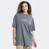 Remera de corte oversize color gris, con cuello redondo y mangas cortas. Presenta un estampado pequeño en el centro del pecho con motivos florales y de frutas en color rosado.