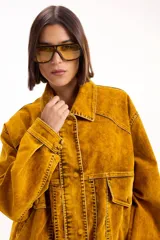 Campera tipo denim oversized en tono ocre lavado, con cuello camisero, cierre frontal de botones, bolsillos frontales con solapa y costuras marcadas en contraste.