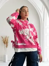Buzo con capucha color fucsia y blanco con estampado tie-dye, cordones ajustables y lazos decorativos en los laterales.
