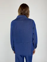 Chaqueta marrón con cuello camisero, cierre frontal con botones, bolsillos de parche y ruedo desflecado.