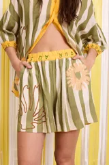 Short con estampado a rayas verticales en tonos verde y blanco, con cintura elastizada y detalle de estampado floral y texto.