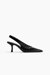 Zapato destalonado negro con textura de cocodrilo, punta fina y taco bajo/medio de forma curva. Posee una tira elástica en el talón para ajuste.