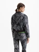 Chaqueta estilo bomber confeccionada en gabardina con estampado de damasco. Presenta cierre frontal oculto por carterón, bolsillos con tapa en forma de V y detalles tejidos en cuello y ruedo.