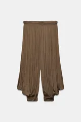 Pantalón bombacho de tiro bajo color marrón, confeccionado en tejido plisado con acabado satinado. Presenta perneras amplias y abullonadas con puños ajustados en los tobillos y cierre lateral con cremallera oculta.