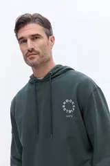 Canguro con capucha de algodón color beige, con cordones de ajuste y estampa circular frontal con el nombre de la marca y el año 1971.