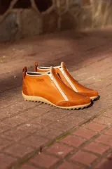 Zapato bajo de cuero color beige con refuerzos en gamuza en la puntera y el talón. Cuenta con doble cierre lateral diagonal, presilla trasera y suela de goma con relieve.