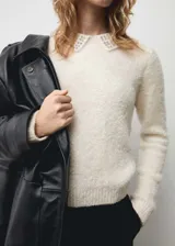 Jersey de punto de textura suave en color crudo, con cuello polo decorado con aplicaciones de strass y manga larga.