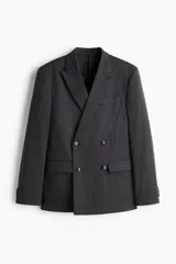 Blazer cruzado de tejido gris oscuro con finas rayas verticales blancas (pinstripe). Presenta solapas de pico, cierre de doble botonadura con botones oscuros, bolsillo superior insertado y dos bolsillos delanteros ribeteados con solapa. Tiene botones decorativos en los puños y abertura trasera.