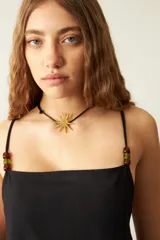 Collar con cordón negro y dije dorado con forma de estrella irregular.