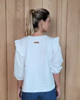 Remera blanca de algodón con cuello redondo, mangas tres cuartos abullonadas y detalle de volados en los hombros.